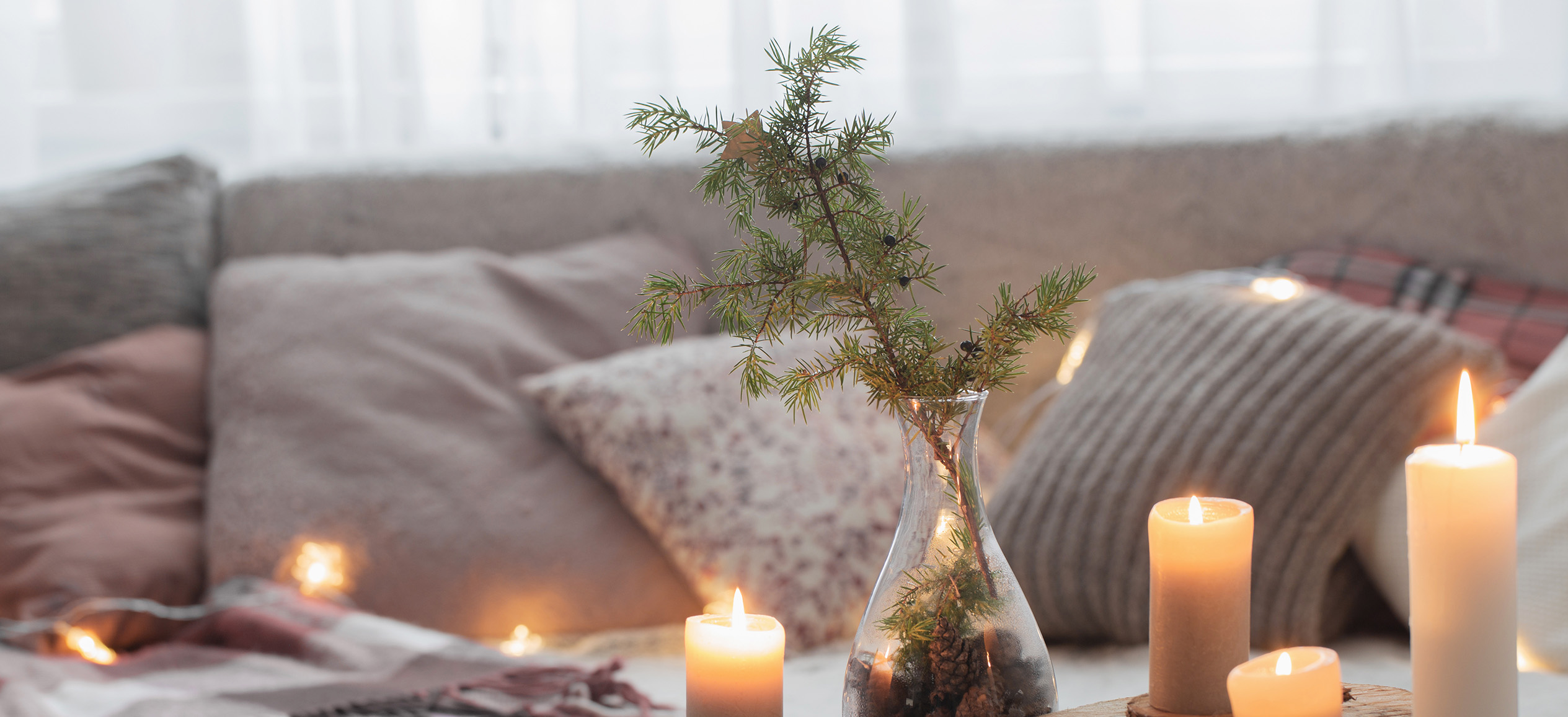 Cozy living room with lit candles, a couch, and a vase with a pine tree branch in it