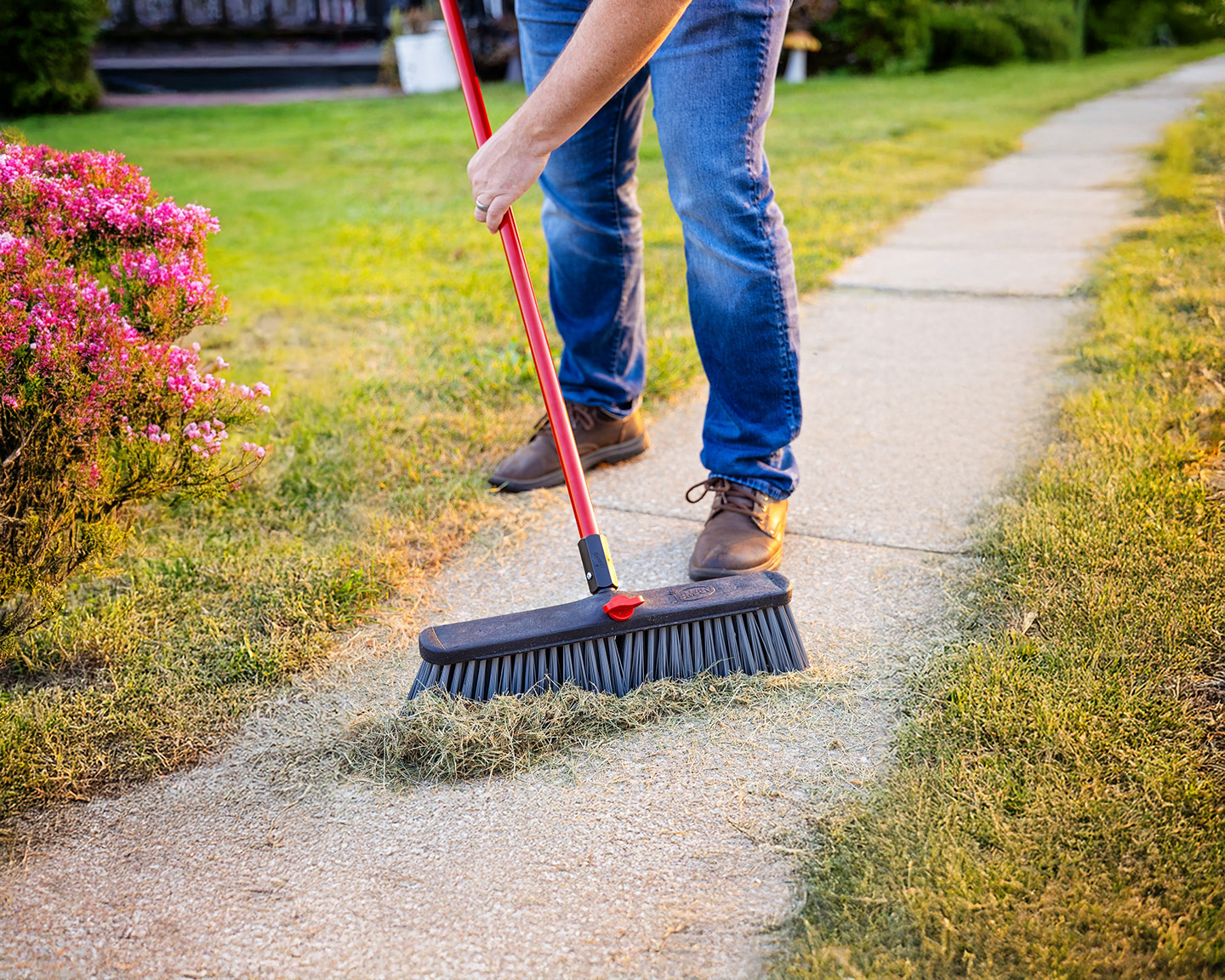 Person sweeping up grass on a sidewalk
