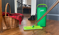 Mop and bucket on wood floor next to a basket with a red blanket