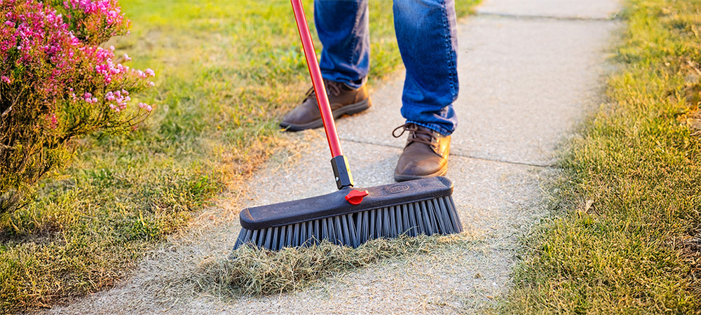Person sweeping up grass on a sidewalk