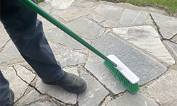 Person sweeping up outdoor patio with small push broom
