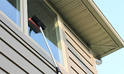 Extended handle with a squeegee head being used to clean an exterior window
